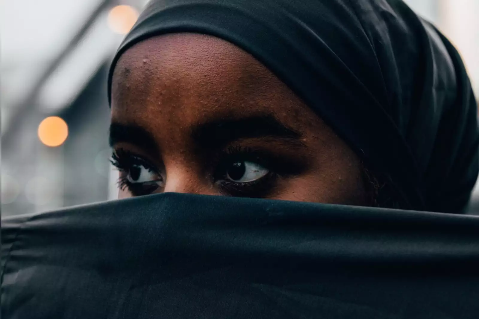 A close-up of Ebyan, whose mouth is covered by a black veil stretched in front of her face.
