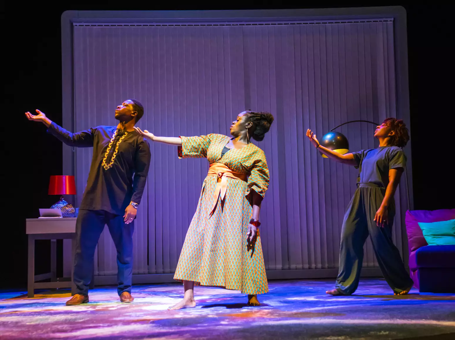 Itoya Osagiede, Michelle Asante and Uche Abuah on stage in Notes on Grief. All three stand on the stage in a line striking the same pose, facing forward, twisting to the right with their right arm raised to shoulder height and their face turned towards their raised hand.