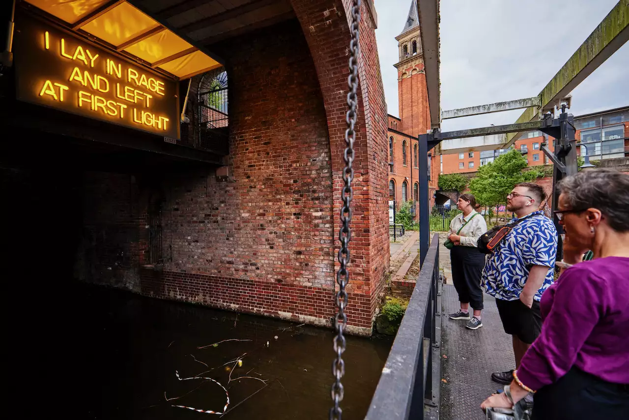 Photo of people looking at a sign that reads 'I lay in rage and left at first light'
