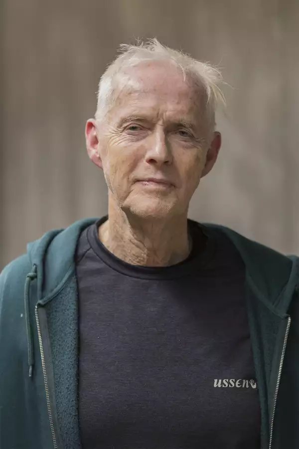Portrait photograph of Bernard Leach wearing a black t-shirt and blue-green hooded jacket